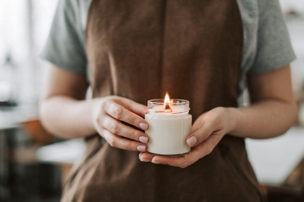 pexels-photo-6755862 Close-up of hands holding a lit handmade candle in a workshop setting, symbolizing craftsmanship.